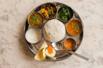 A traditional Nepali khana set featuring rice, lentil soup (dal), vegetables, pickles, and curry.