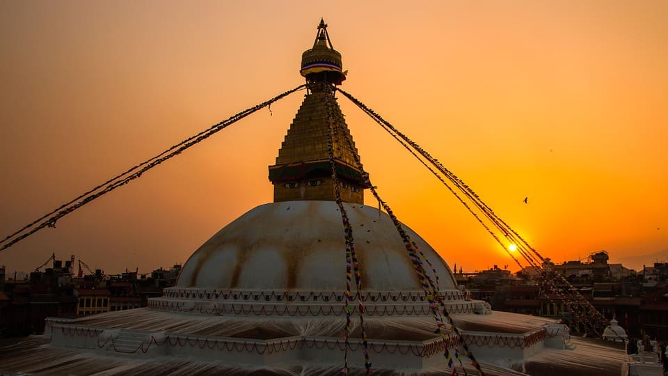 Boudhanath Stupa in Kathmandu, Nepal, glowing during sunset with vibrant colors reflecting on its golden dome and surrounding prayer flags.