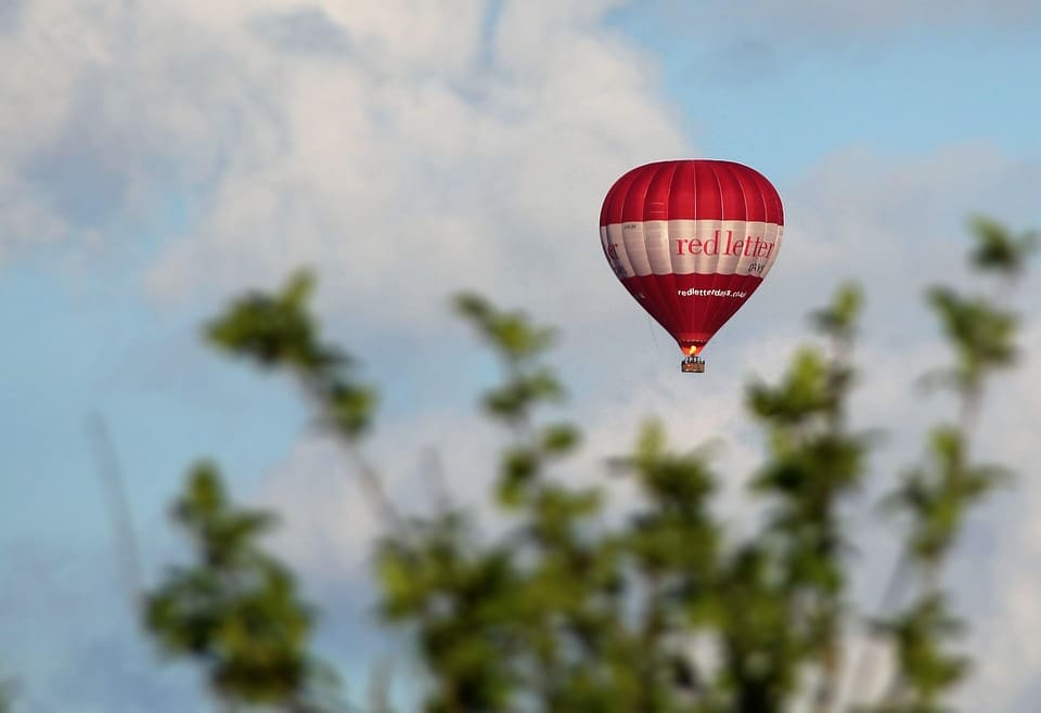 Colorful hot air balloon floating over scenic landscapes, offering a panoramic view of mountains, valleys, and clear skies.